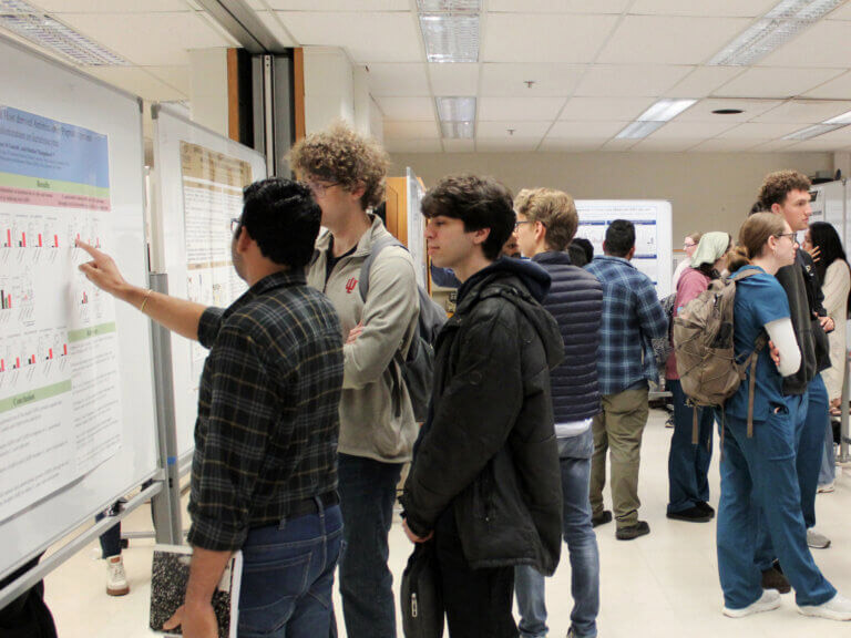 People gather in a hallway to view and discuss research posters.